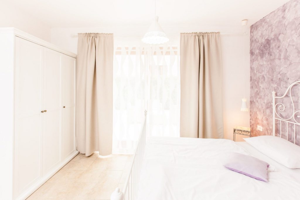 Das romantische Schlafzimmer mit dem Metallbett hat einen direkten Zugang zur großen Terrasse. Gegenüber von dem Doppelbett steht ein großer Kleiderschrank.