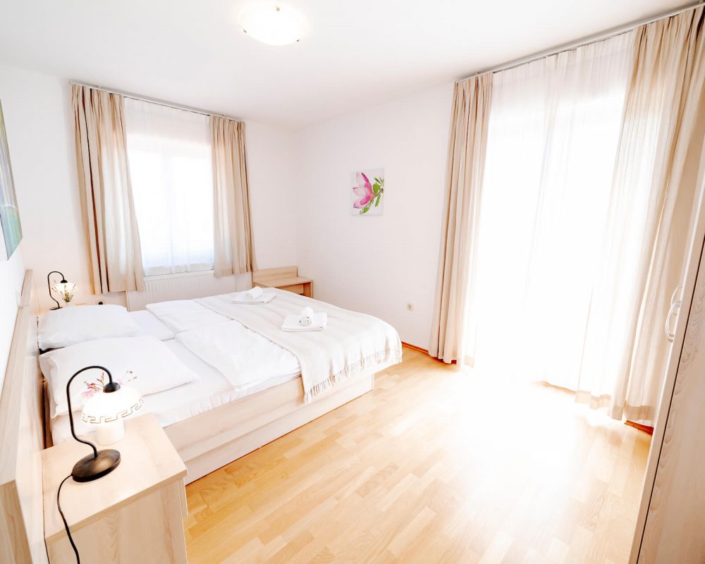 Das Ferienhaus Villa Alma hat ein Schlafzimmer mit einem schicken Doppelbett, zwei Nachttischen und hellen Gardinen.