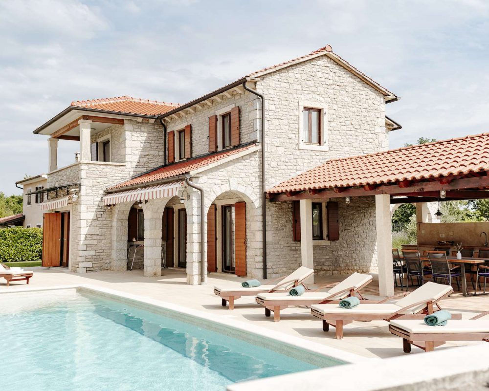 Der erfrischende Swimmingpool der Villa verfügtüber einen kleinen, eleganten Wasserfall. Auf der Terrasse stehen Sonnenliegen um den Pool.