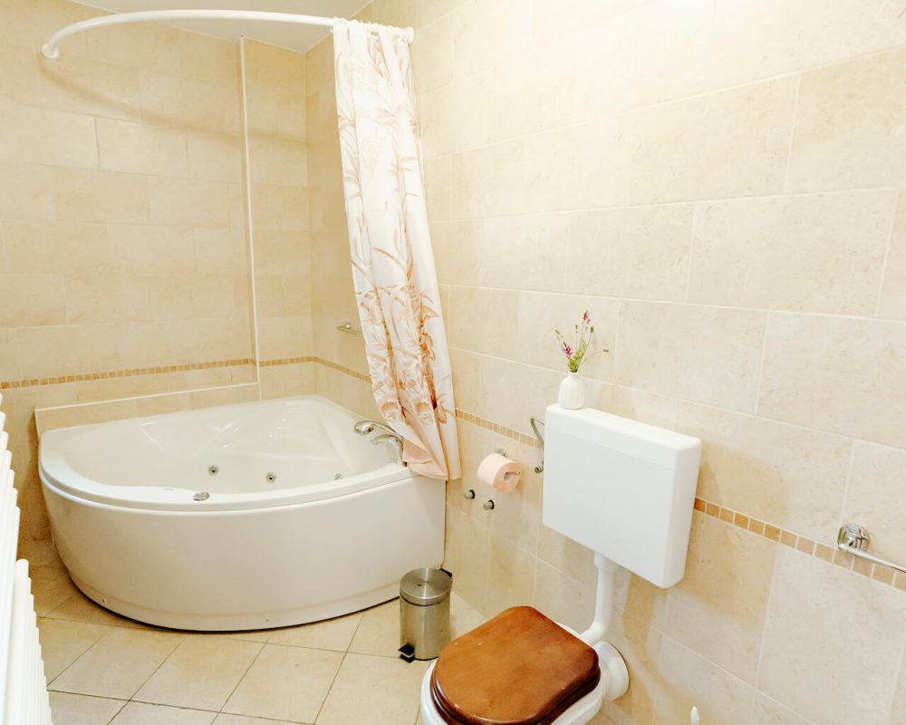 In dem großen Badezimmer steht ein kleiner quadratischer Badschrank, eine Dusche und eine große Eckbadewanne.