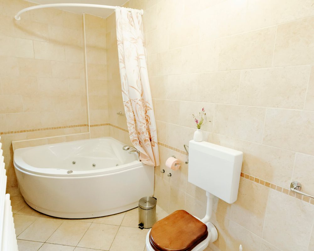 In dem großen Badezimmer steht ein kleiner quadratischer Badschrank, eine Dusche und eine große Eckbadewanne.