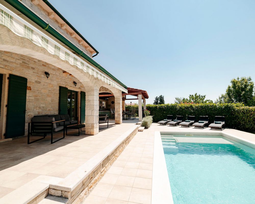 Auf der überdachten Terrasse stehen bequeme Loungemöbel. Von dort aus hat man einen tollen Blick auf den Swimmingpool und die Natur.